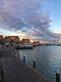 Pier on harbor by buildings against sky during sunset