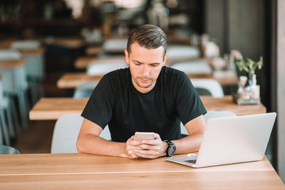 Man using mobile phone while sitting on table at cafe