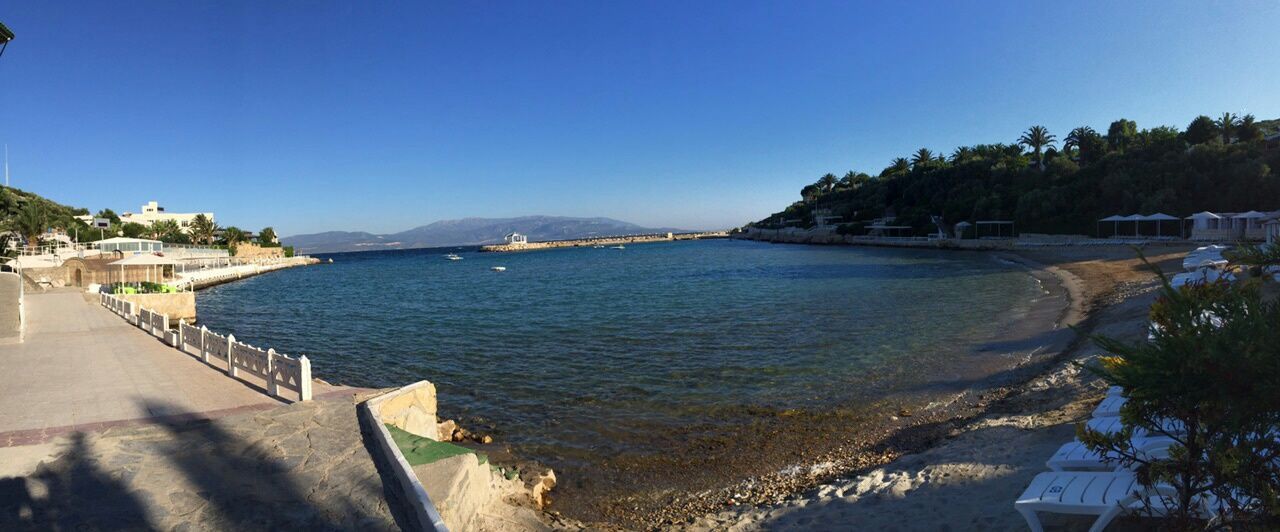 clear sky, water, sea, blue, copy space, beach, built structure, scenics, tranquil scene, tree, mountain, tranquility, sunlight, building exterior, beauty in nature, nature, architecture, sand, day, shore