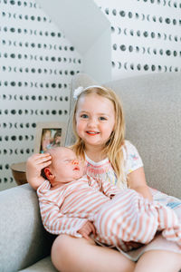 A young girl smiling at the camera while holding her baby sister