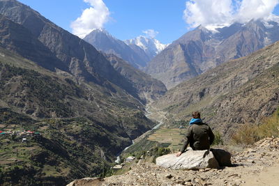 Rear view of man sitting on mountain against sky