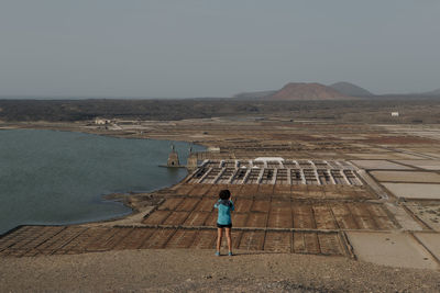 Rear view of man walking on beach against clear sky