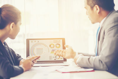 Businessman pointing at laptop while colleague sitting on table