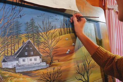 Cropped hand of woman drawing on canvas in cottage
