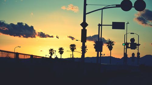 Low angle view of silhouette palm trees and poles against sky during sunset