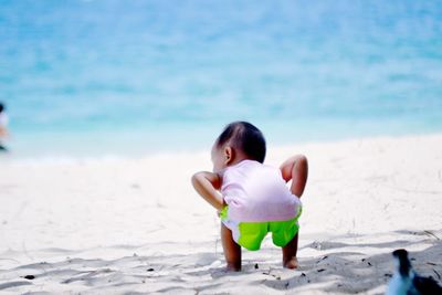 Rear view of baby boy crouching on sand at beach against sky