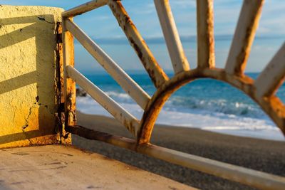Close-up of metallic railing at beach against sky