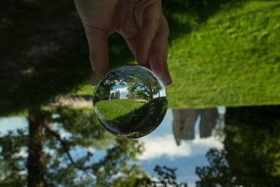 Close-up of hand holding crystal ball against trees