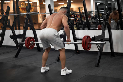 Rear view of shirtless man exercising at gym