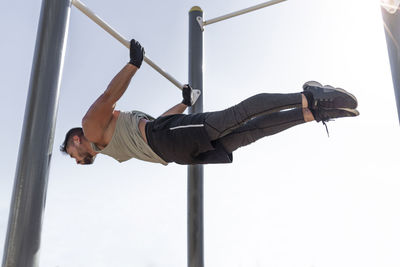 Male athlete exercising on horizontal bar at park against clear sky