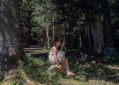 Girl sitting on tree trunk in forest