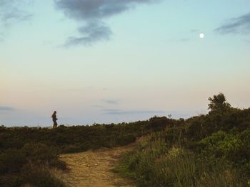 Man standing amidst grass against sky at dusk