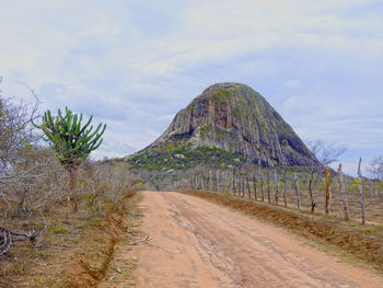 Dirt road by mountain against sky