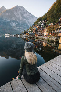Rear view of woman sitting on pier over lake against mountains