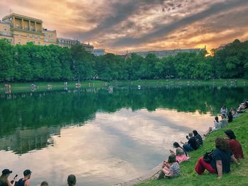 People sitting by lake against sky