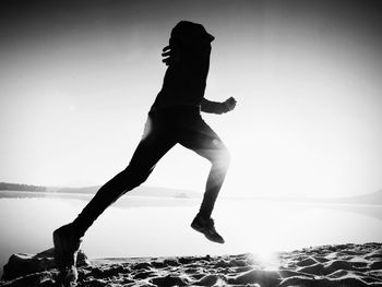 Full length of silhouette man jumping in sea against clear sky