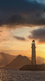 Lighthouse by sea against sky during sunset