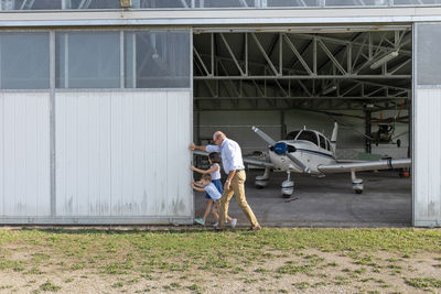 Children and grandfather opening door of airplane hangar