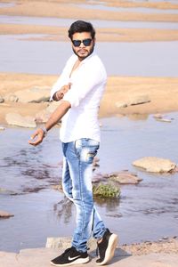 Portrait of man in sunglasses folding sleeve at beach