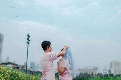 Man adjusting veil on woman head against sky