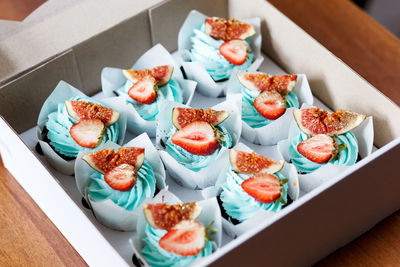 The plate of tasty cupcakes decorated with strawberry, fig and cream