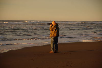 Rear view of man standing on beach during sunset