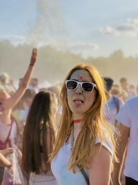 Portrait of young woman with sunglasses sticking out tongue at music festival