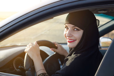 Portrait of woman wearing hijab driving in car seen through window