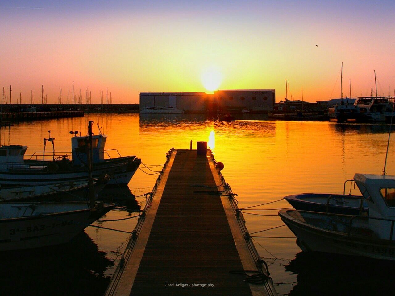 sunset, water, sun, nautical vessel, transportation, moored, boat, sea, mode of transport, built structure, clear sky, sunlight, orange color, architecture, reflection, pier, building exterior, jetty, harbor, sky