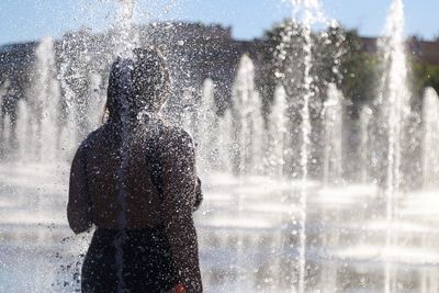 Rear view of woman standing amidst fountain