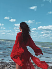 Rear view of woman standing at beach against sky