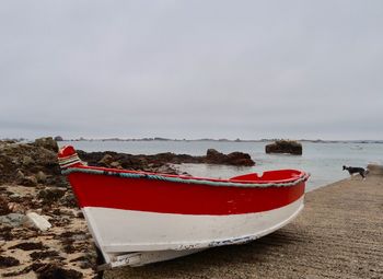 Red boat moored on beach against sky