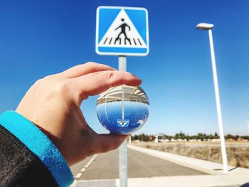 Cropped hand holding crystal ball with reflection against road sign