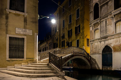 Bridge over canal amidst buildings in city at night