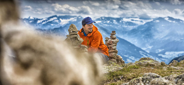 Young man sitting amidst stacks of rocks on mountain