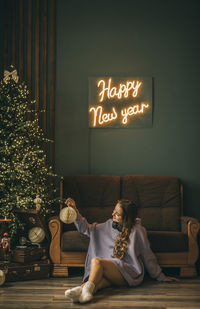 Young woman, headphones listens music on vinyl record, sits on floor near christmas tree 