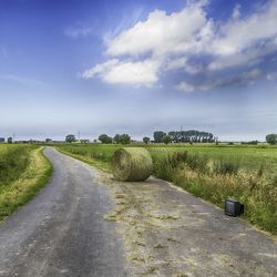 Hay bale and abandoned television on road amidst grassy field