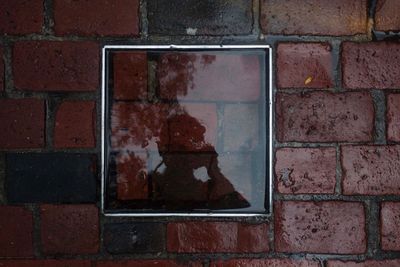 Reflection of person on square shape puddle at footpath during rainy season