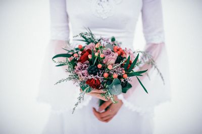 Midsection of bride holding bouquet against white background