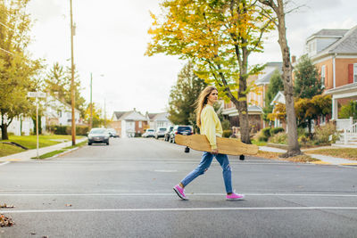 Side view of girl with long hair crossing the street while holding a longboard