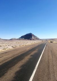 Road leading towards mountains against clear blue sky