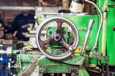 A close-up of a metallic green old lathe with an adjusting valve at an industrial plant