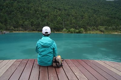 Rear view of man sitting on pier over lake against trees