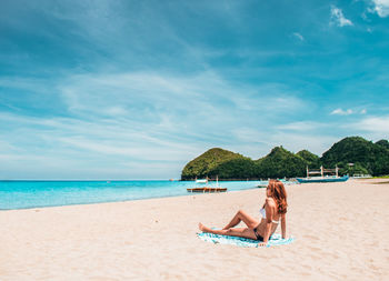 Man relaxing on beach against sky