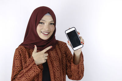 Portrait of smiling young woman using smart phone against white background