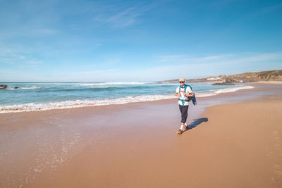 Rear view of woman walking at beach against sky