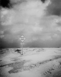 Road sign on snow covered landscape against sky