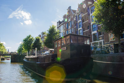 Boats moored in canal by city against sky