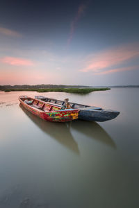 Boat moored on sea against sky during sunset