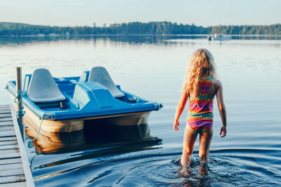 Blonde girl walking to pedal boat in lake water on sunset. summer sport water outdoor activity. 